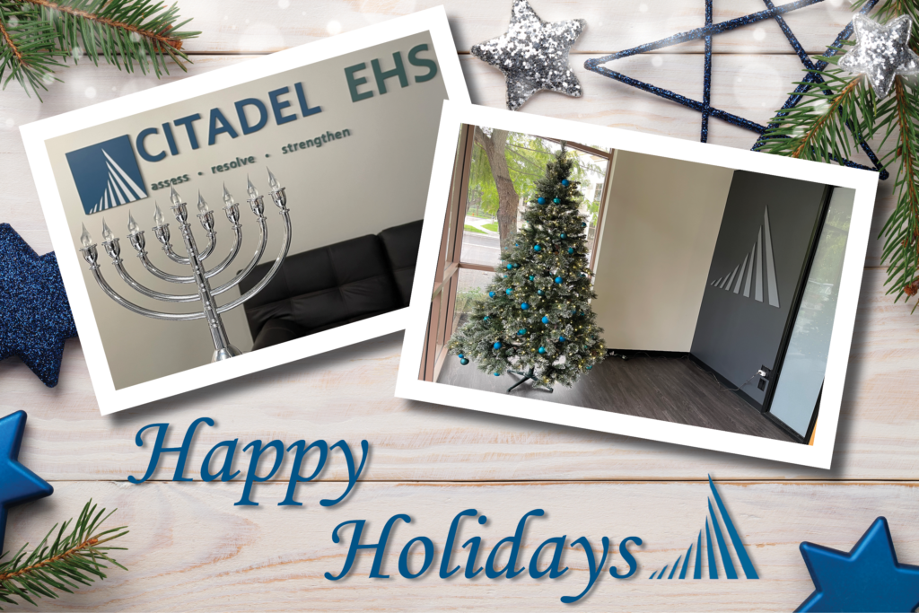 A light wooden table with evergreen trimmings and blue and silver star ornaments. on the table are two poloroid style images of the Citadel EHS office decorations, one with a menorah and one with a christmas tree. Blue text across the bottom reads "Happy Holidays" 