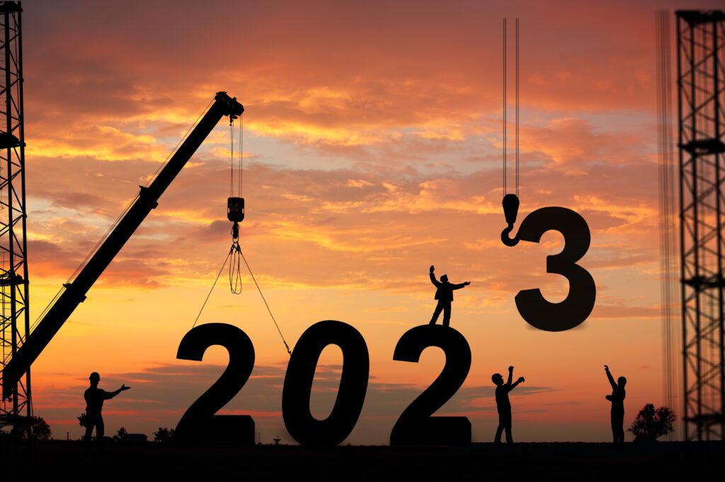 Happy New Year! An image of silhouettes of a construction crew craning in the numbers 2023 with a sunset background.